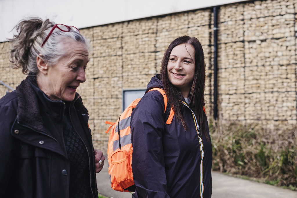 Two women walking on a path carrying orange backpacks